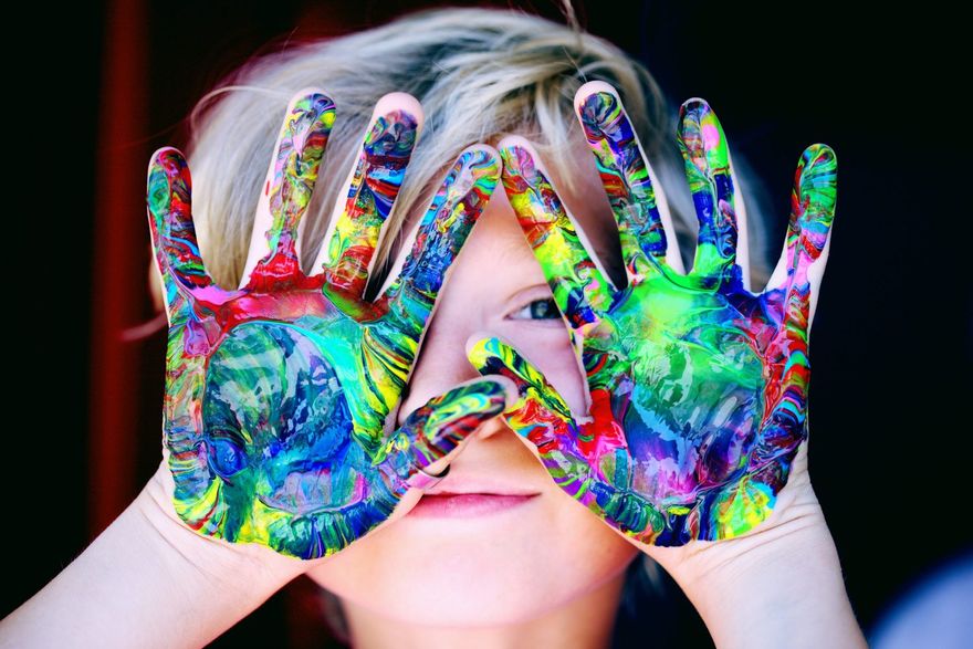 Niño con las manos pintadas de colores sobre los ojos