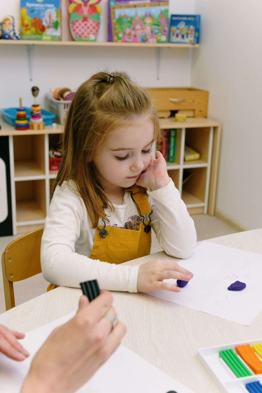 Niña trabaja motricidad fina con plastilina mientras la terapeuta registra datos