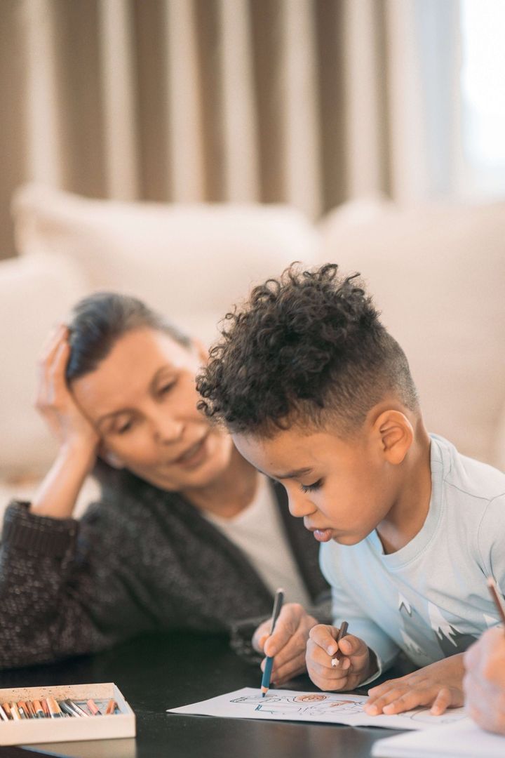Caregiver watches a young boy draw at home