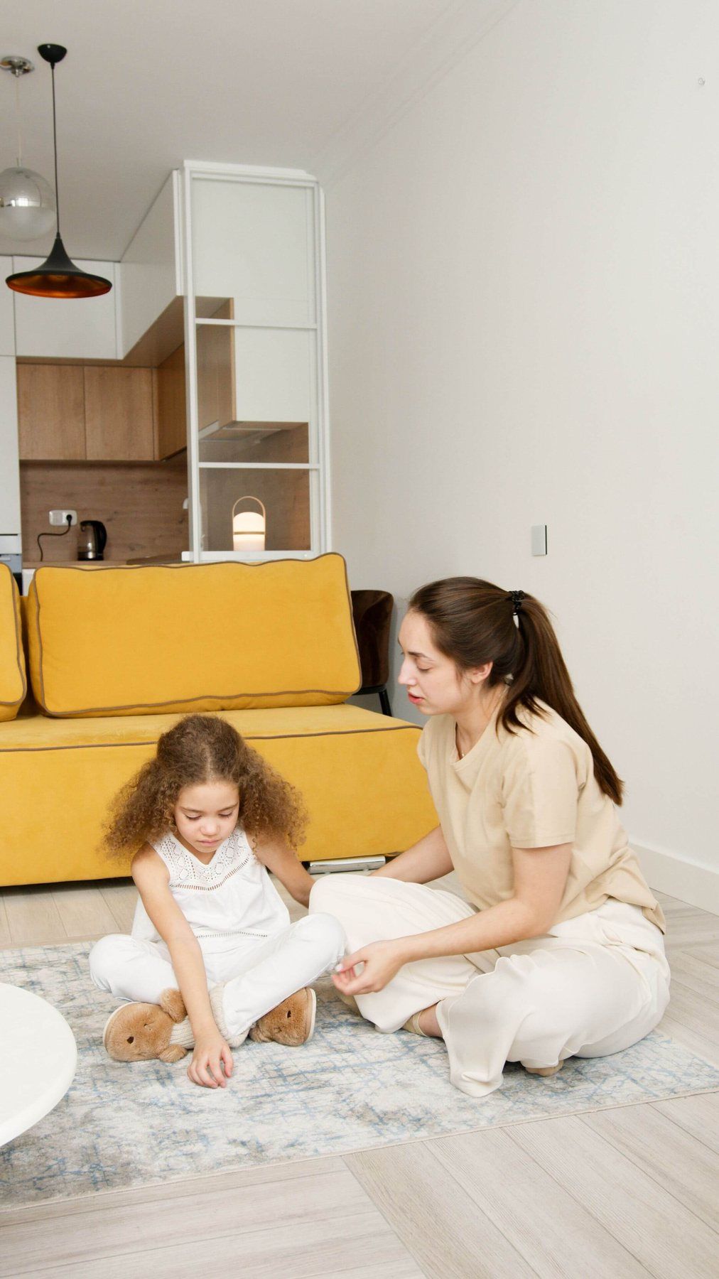 Therapist sits on the living-room floor with a young girl during an in-home ABA session