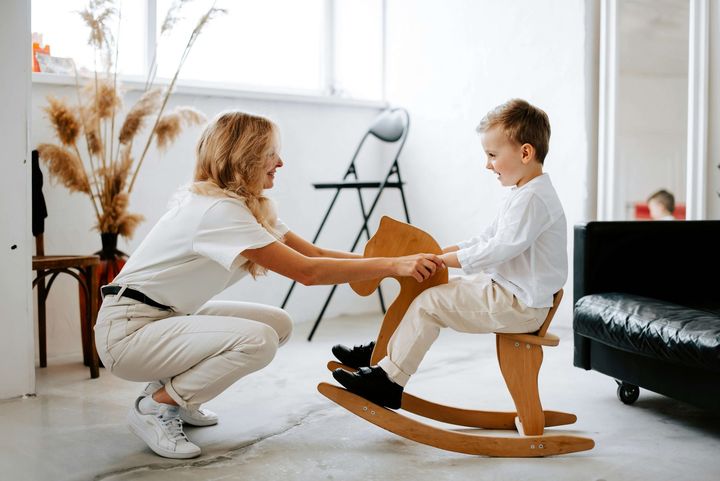 Smiling therapist plays with a laughing boy on a rocking horse