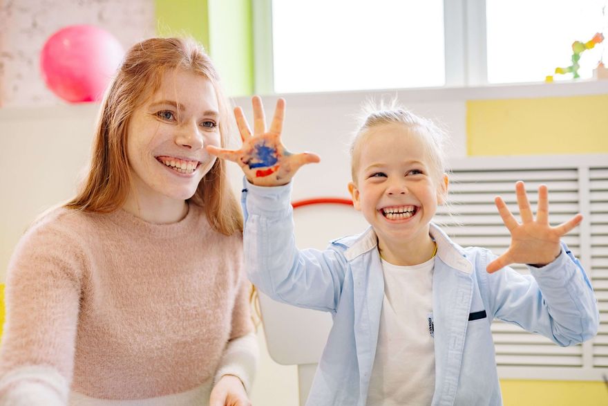 Therapist and boy laugh together, showing paint-covered hands