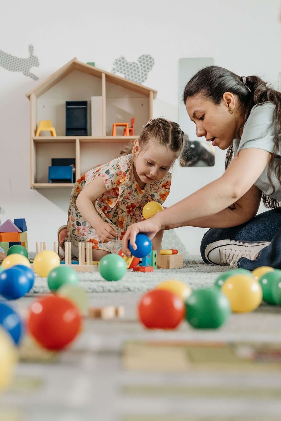 Terapeuta y niña juegan con pelotas de colores en el piso de un cuarto de juegos